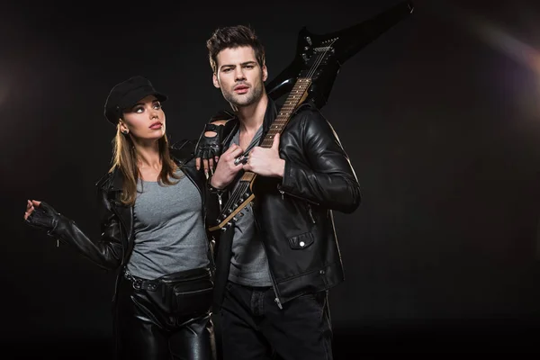Beautiful couple in leather jackets posing with electric guitar on black background — Stock Photo