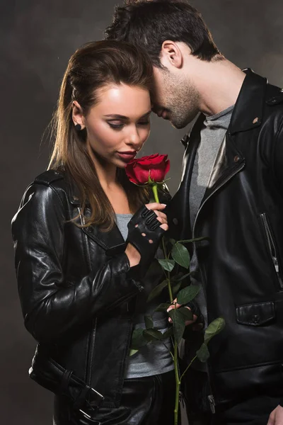 Hermosa pareja en chaquetas de cuero posando con rosa roja sobre fondo oscuro - foto de stock