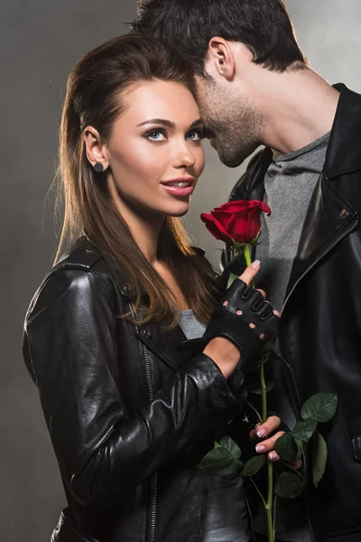 Hermosa pareja en chaquetas de cuero posando con rosa roja sobre fondo gris — Stock Photo