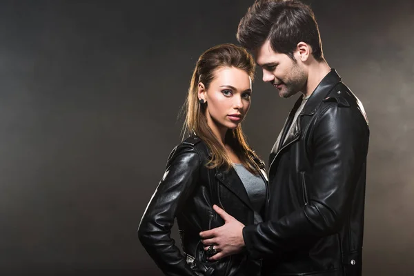 Beautiful couple in leather jackets embracing on dark background with copy space — Stock Photo