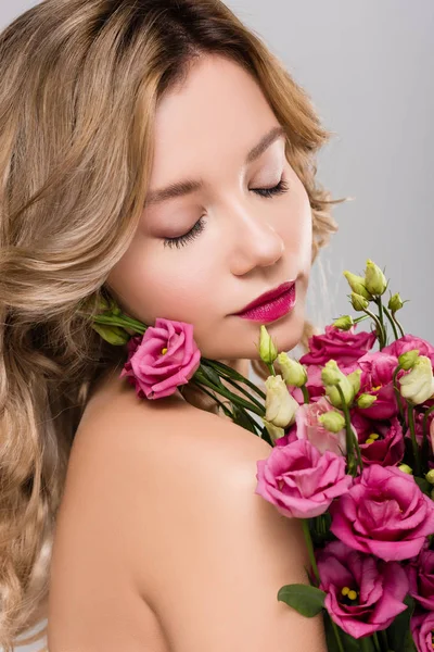 Naked beautiful blonde woman with closed eyes posing with spring Eustoma flowers bouquet isolated on grey — Stock Photo