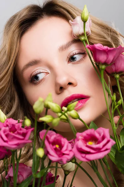 Nahaufnahme einer schönen jungen Frau, die sich hinter einem Strauß Eustoma-Blumen versteckt, isoliert auf grau — Stockfoto