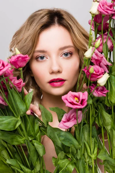 Close up of beautiful spring young woman looking through Eustoma flowers isolated on grey — Stock Photo