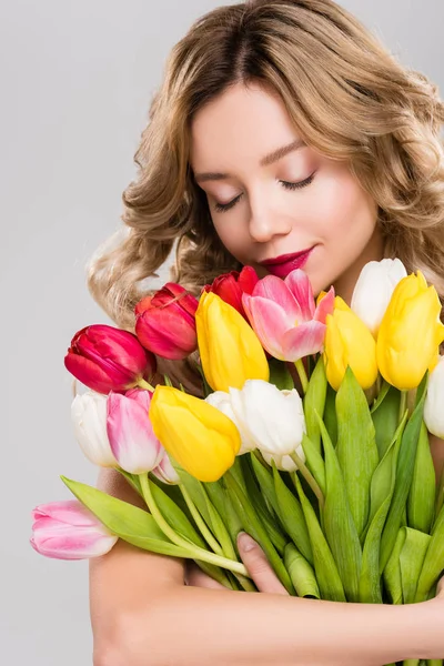 Junge attraktive Frühlingsfrau mit geschlossenen Augen hält Strauß bunter Tulpen isoliert auf grau — Stockfoto