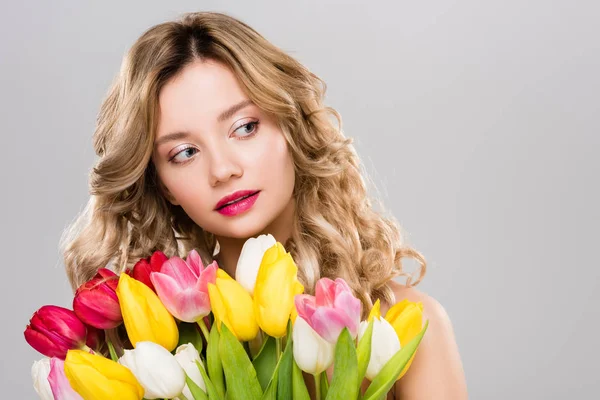 Junge attraktive Frühlingsfrau hält Strauß bunter Tulpen in der Hand und schaut isoliert auf grau — Stockfoto