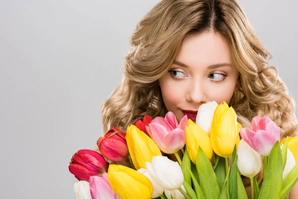 Молода красива весняна жінка тримає букет з різнокольорових тюльпанів ізольовані на сірому — стокове фото
