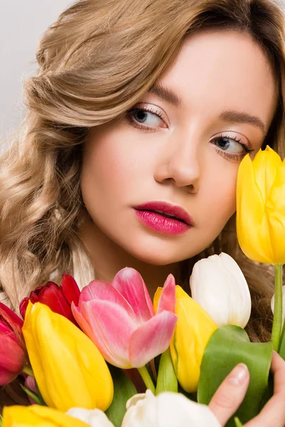 Close up of young attractive spring woman holding bouquet of colorful tulips isolated on grey — Stock Photo