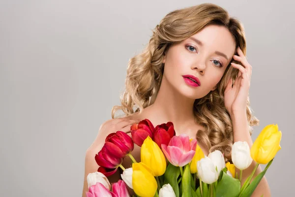 Giovane donna nuda primavera tenendo bouquet di tulipani colorati e toccando i capelli isolati su grigio — Foto stock