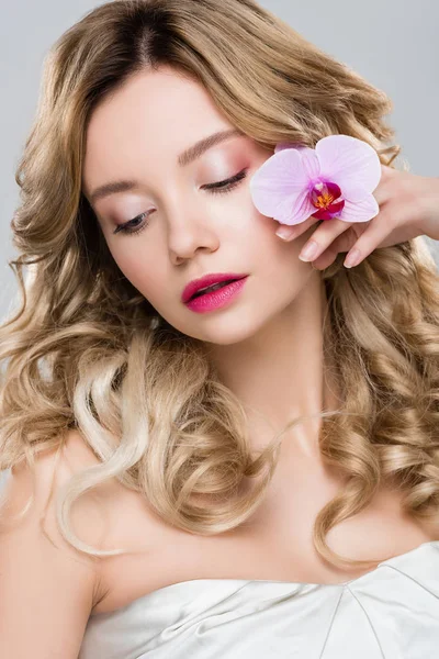 Junge Frau hält lila Orchidee nahe Gesicht isoliert auf grau — Stockfoto