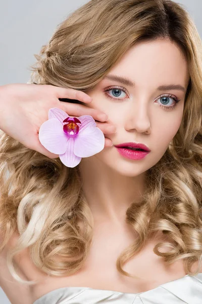 Young blonde attractive woman holding purple orchid in palm isolated on grey — Stock Photo