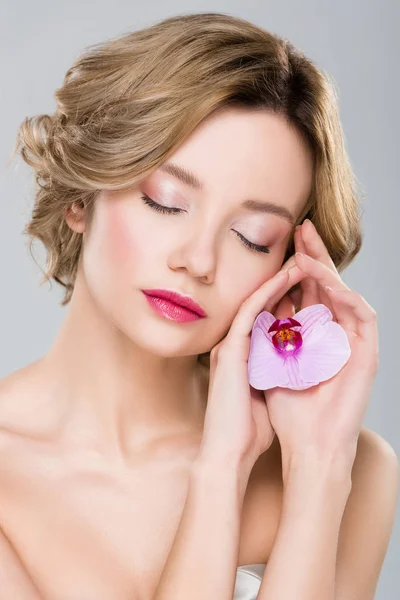 Portrait of young tender woman with closed eyes holding purple orchid isolated on grey — Stock Photo