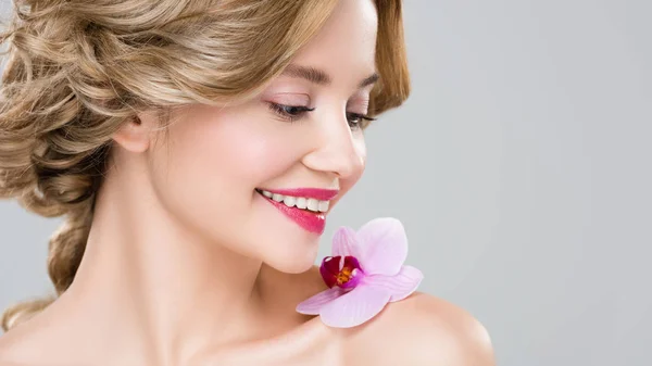 Portrait of young smiling naked woman with purple orchid on shoulder isolated on grey — Stock Photo