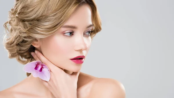 Young tender naked woman touching neck with purple orchid on hand isolated on grey — Stock Photo
