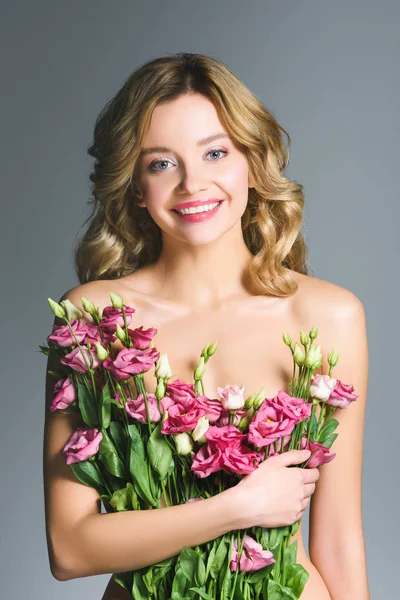 Happy naked woman holding bouquet of eustoma flowers isolated on grey — Stock Photo