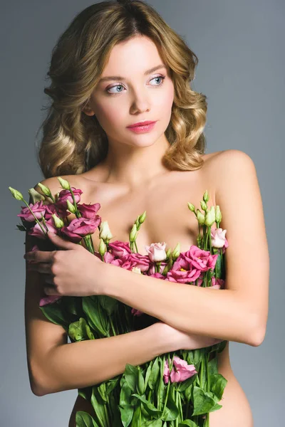 Bonita chica desnuda sosteniendo ramo de flores de eustoma aisladas en gris - foto de stock