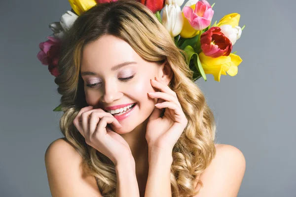 Усміхнена дівчина з вінком квітів на волоссі ізольована на сірому — стокове фото