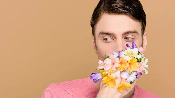 Mann bedeckt Mund mit Alstroemeria-Blüten an der Hand isoliert auf beige — Stockfoto