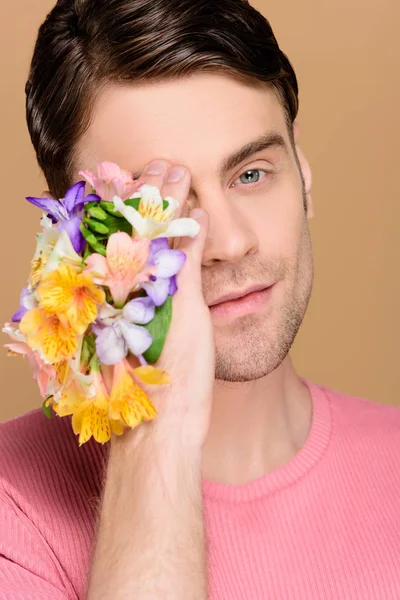 Handsome man covering one eye with flowers on hand isolated on beige — Stock Photo