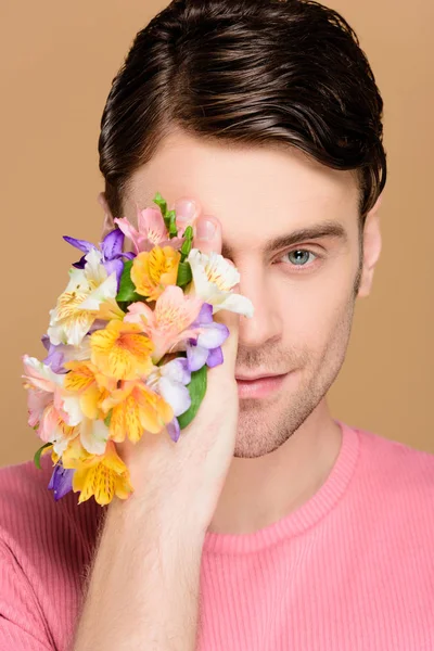 Cheerful man covering one eye with flowers on hand isolated on beige — Stock Photo