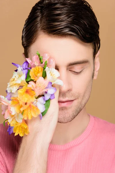 Bell'uomo con gli occhi chiusi che coprono un occhio con i fiori a portata di mano isolati su beige — Foto stock