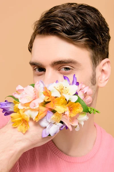 Mann bedeckt Mund mit Alstroemeria-Blüten an der Hand isoliert auf beige — Stockfoto