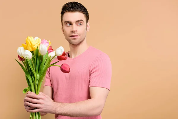 Здивований чоловік тримає букет тюльпанів ізольований на бежевому — стокове фото