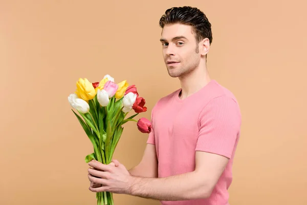 Hombre guapo sosteniendo ramo de flores aisladas en beige - foto de stock