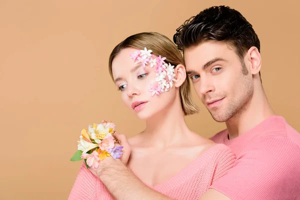 Handsome boyfriend hugging girlfriend with flowers on face isolated on beige — Stock Photo