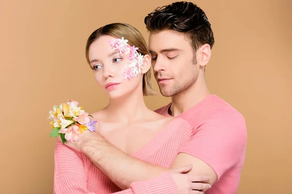 Schöner Mann umarmt attraktive Freundin mit Blumen im Gesicht isoliert auf beige — Stockfoto