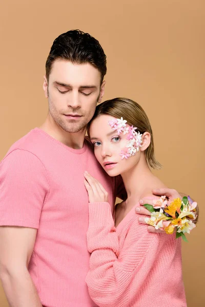 Hombre abrazando atractiva novia con flores en la cara aislado en beige - foto de stock