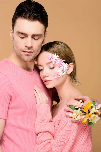 Guapo hombre abrazando novia con flores en la cara aislado en beige - foto de stock