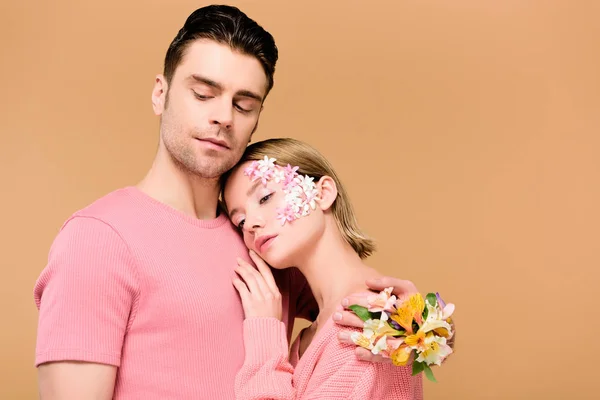 Woman embracing handsome man with flowers on hand isolated on beige — Stock Photo