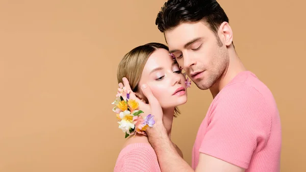 Handsome man with alstroemeria flowers on hand touching face of attractive girlfriend isolated on beige — Stock Photo