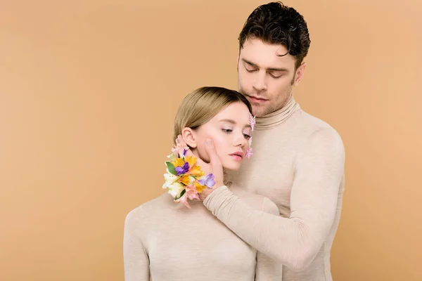 Homem macio com flores alstroemeria na mão tocando rosto de namorada bonita isolado no bege — Fotografia de Stock