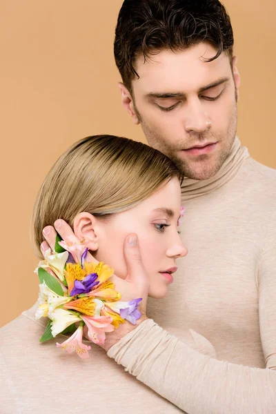 Homem macio com flores alstroemeria na mão tocando rosto de bela namorada isolada no bege — Fotografia de Stock