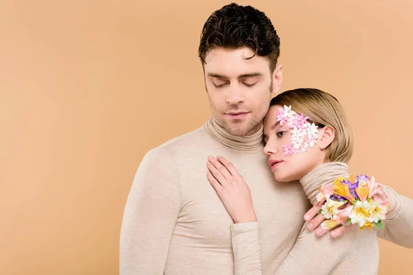 Zarte Frau mit Blumen im Gesicht umarmt gutaussehenden Mann isoliert auf beige — Stockfoto