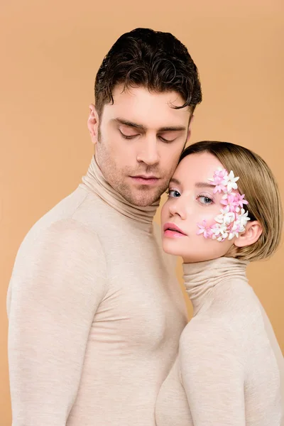 Femme tendre avec des fleurs sur le visage debout avec bel homme isolé sur beige — Photo de stock