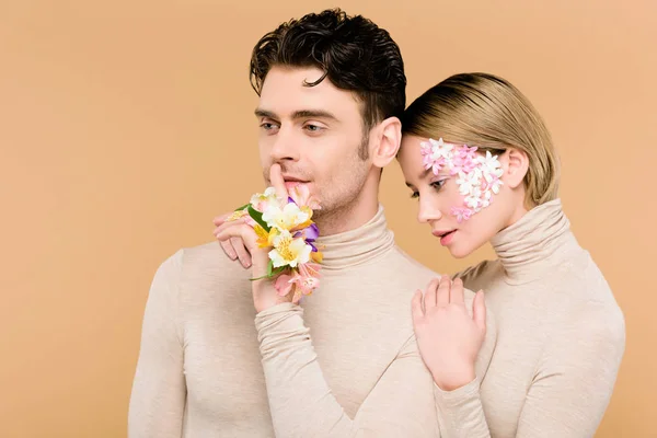 Handsome man standing with pretty girlfriend and showing hush sign isolated on beige — Stock Photo