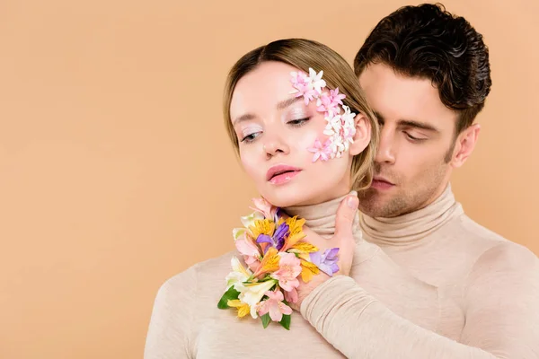 Homme tendre avec des fleurs alstroemeria sur la main toucher le visage de jolie femme isolée sur beige — Photo de stock