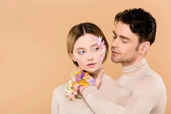Ніжний чоловік з квітами альстромерії на руці торкається обличчя красивої подруги ізольовано на бежевому — стокове фото