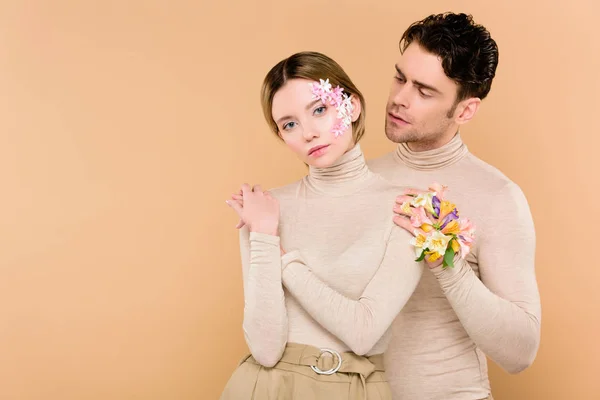 Tierno hombre con flores de alstroemeria en la mano mirando hermosa novia aislada en beige - foto de stock
