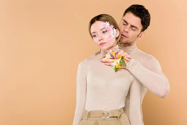 Handsome man with alstroemeria flowers on hand touching neck of beautiful girlfriend isolated on beige — Stock Photo