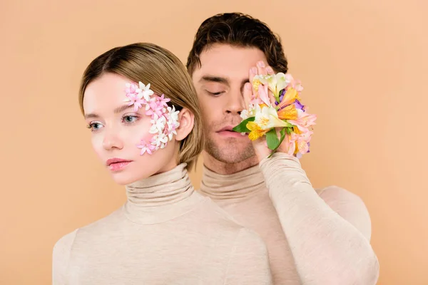 Schöner Mann mit Alstroemeria-Blüten auf der Hand, die ein Auge in der Nähe der schönen Freundin isoliert auf beige bedecken — Stockfoto