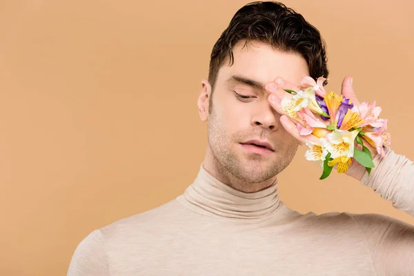 Homme tendre avec des fleurs alstroemeria à la main couvrant un oeil isolé sur beige — Photo de stock