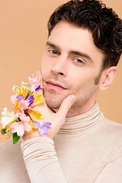 Handsome man with alstroemeria flowers on hand touching face isolated on beige — Stock Photo