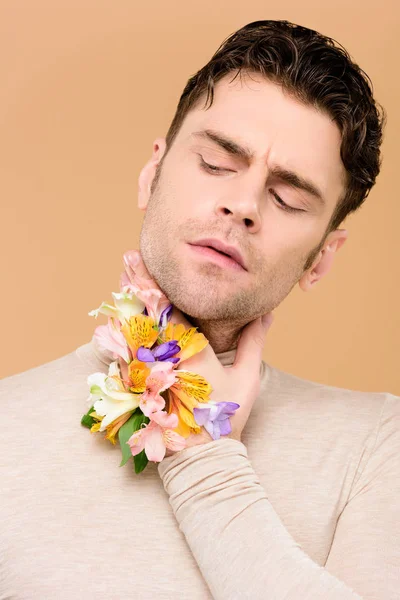 Handsome man with alstroemeria flowers on hand touching neck isolated on beige — Stock Photo