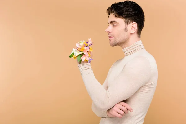 Hombre pensativo con flores de alstroemeria en la mano de pie aislado en beige - foto de stock