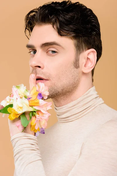 Bel homme avec des fleurs à la main montrant signe de silence isolé sur beige — Photo de stock