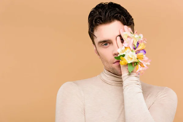 Homem bonito com flores na mão cobrindo um olho isolado no bege — Fotografia de Stock