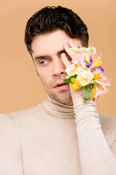 Hombre con flores en la mano cubriendo un ojo aislado en beige - foto de stock